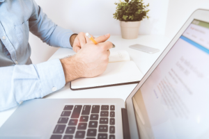 Man holding pen and notebook in front of laptop